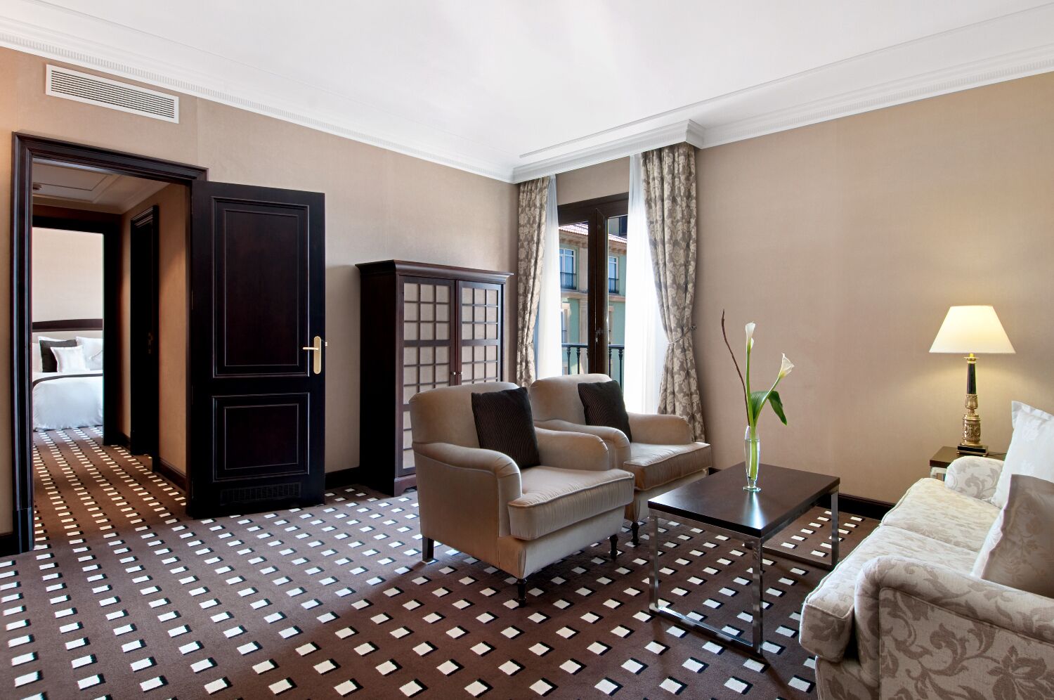 Une chambre d’hôtel avec un sol à motifs, un canapé, un fauteuil, une armoire et une lampe.