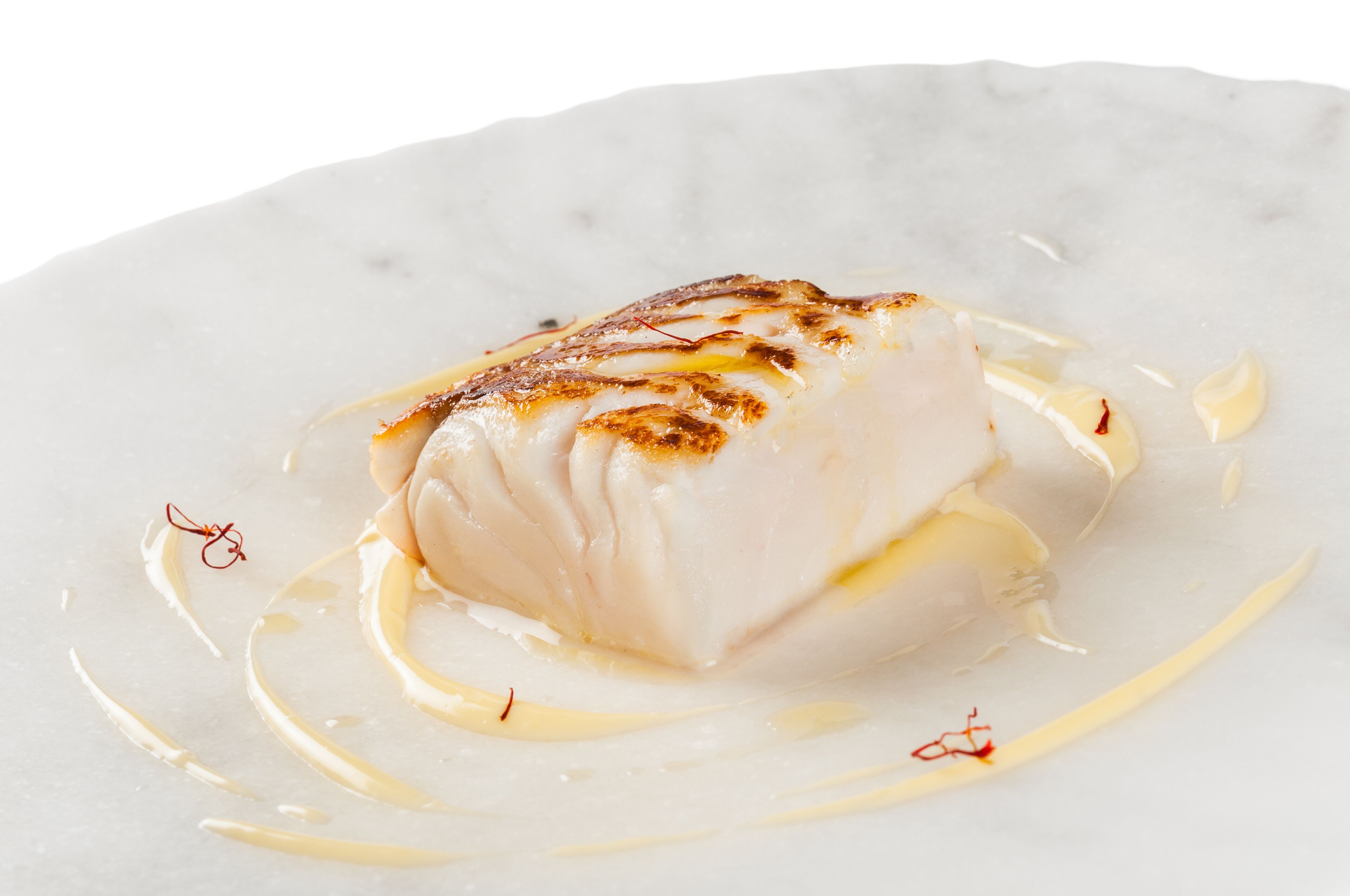 Un plato blanco con un trozo de pescado blanco cubierto por una costra dorada, acompañado de salsa cremosa y adornado con hebras rojas.