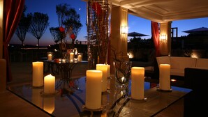 Un comedor con múltiples velas sobre una mesa de vidrio, rodeado de sillas y un centro de mesa decorativo.