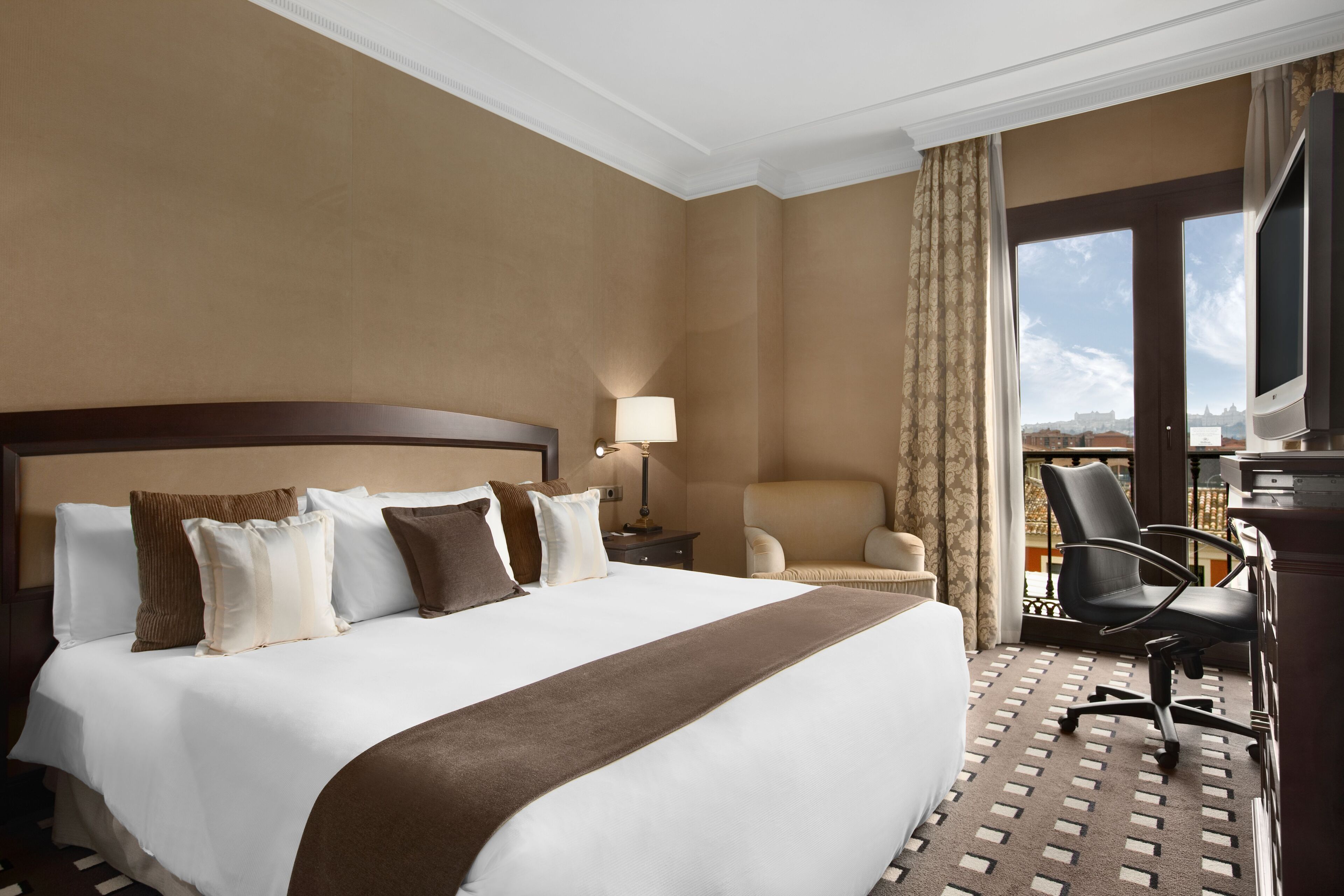 Habitación de hotel con una cama grande, un escritorio, una silla y vista a la ciudad.