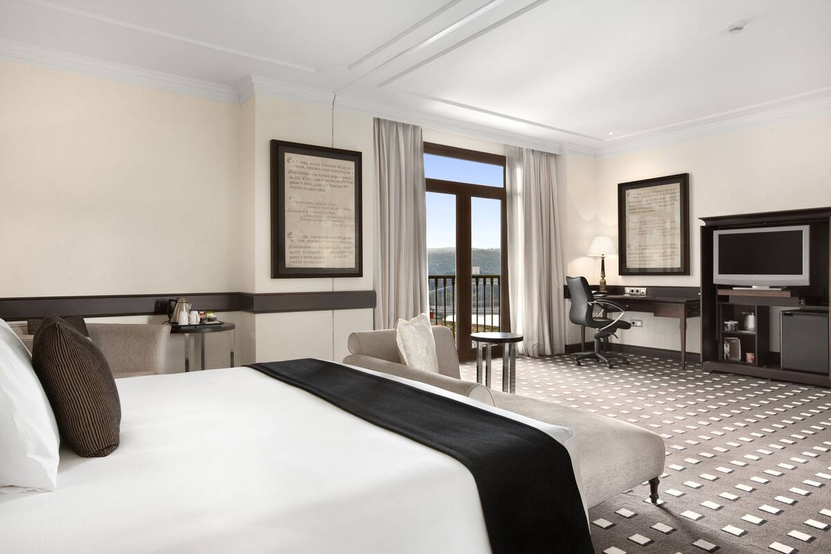 Habitación de hotel con una cama grande, un escritorio, una silla, un televisor y vistas al exterior.