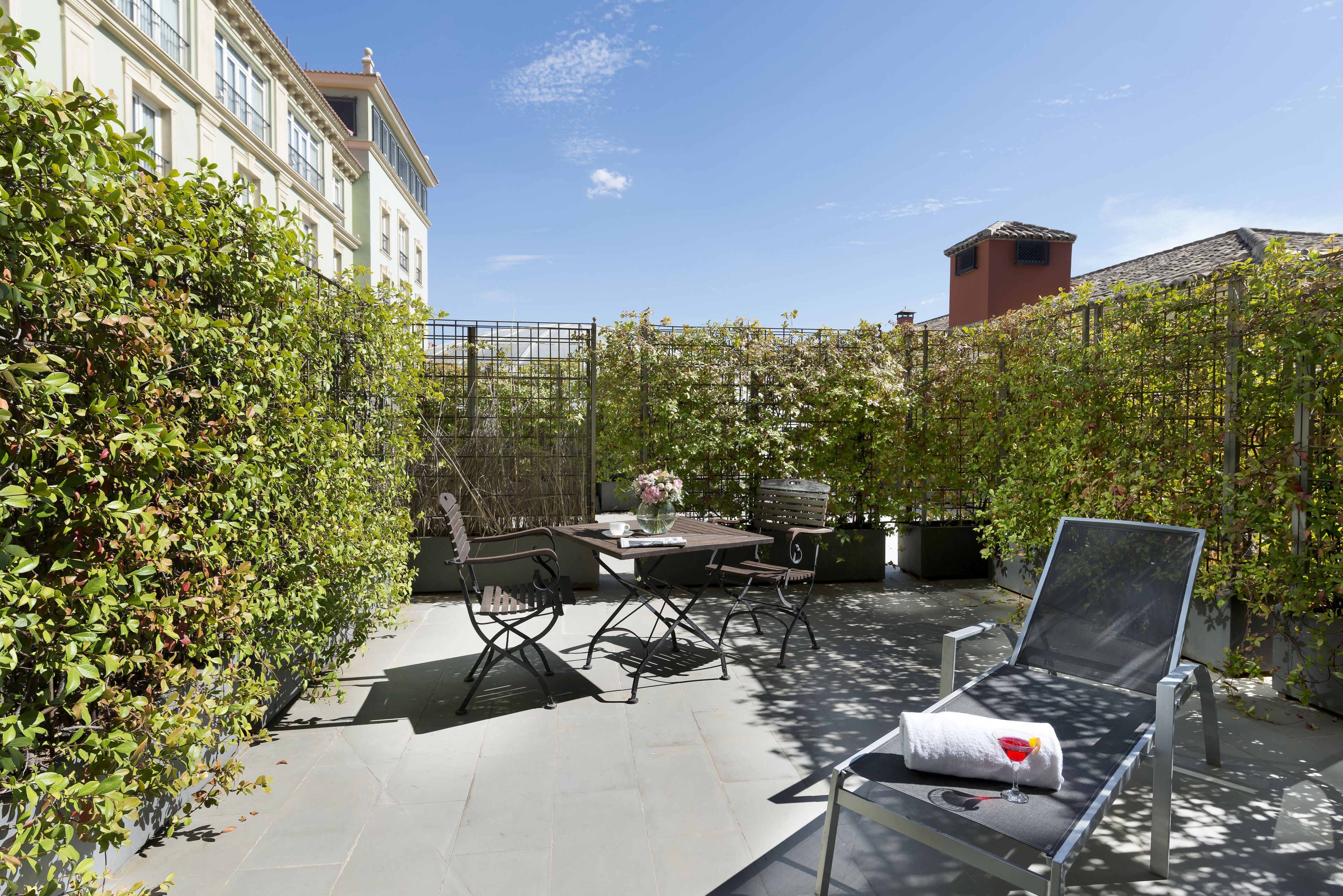 A patio with a table and chairs, a lounge chair, and a view of a building in the background.