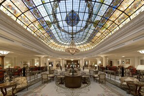 Eine beeindruckende Lobby mit hoher Decke, aufwendigen Buntglasfenstern und einem zentralen Kronleuchter.