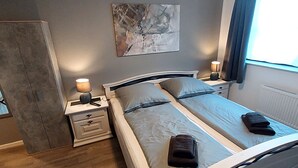 A bedroom with a bed, two bedside tables, a nightstand, a wardrobe, and a window with curtains. - Hotel zum Norden (Jagel)