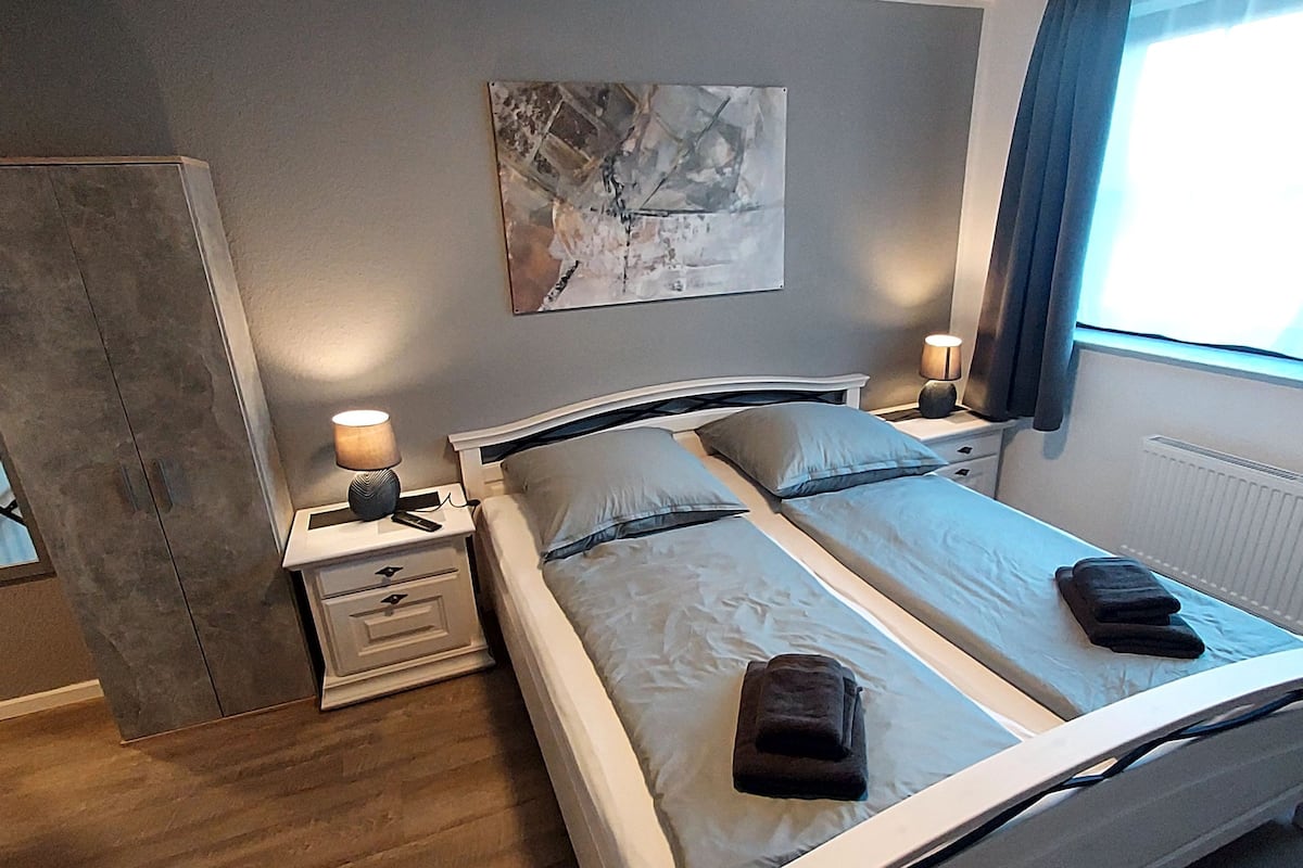Een slaapkamer met een bed, twee nachtkastjes, een kledingkast en een raam met gordijnen.