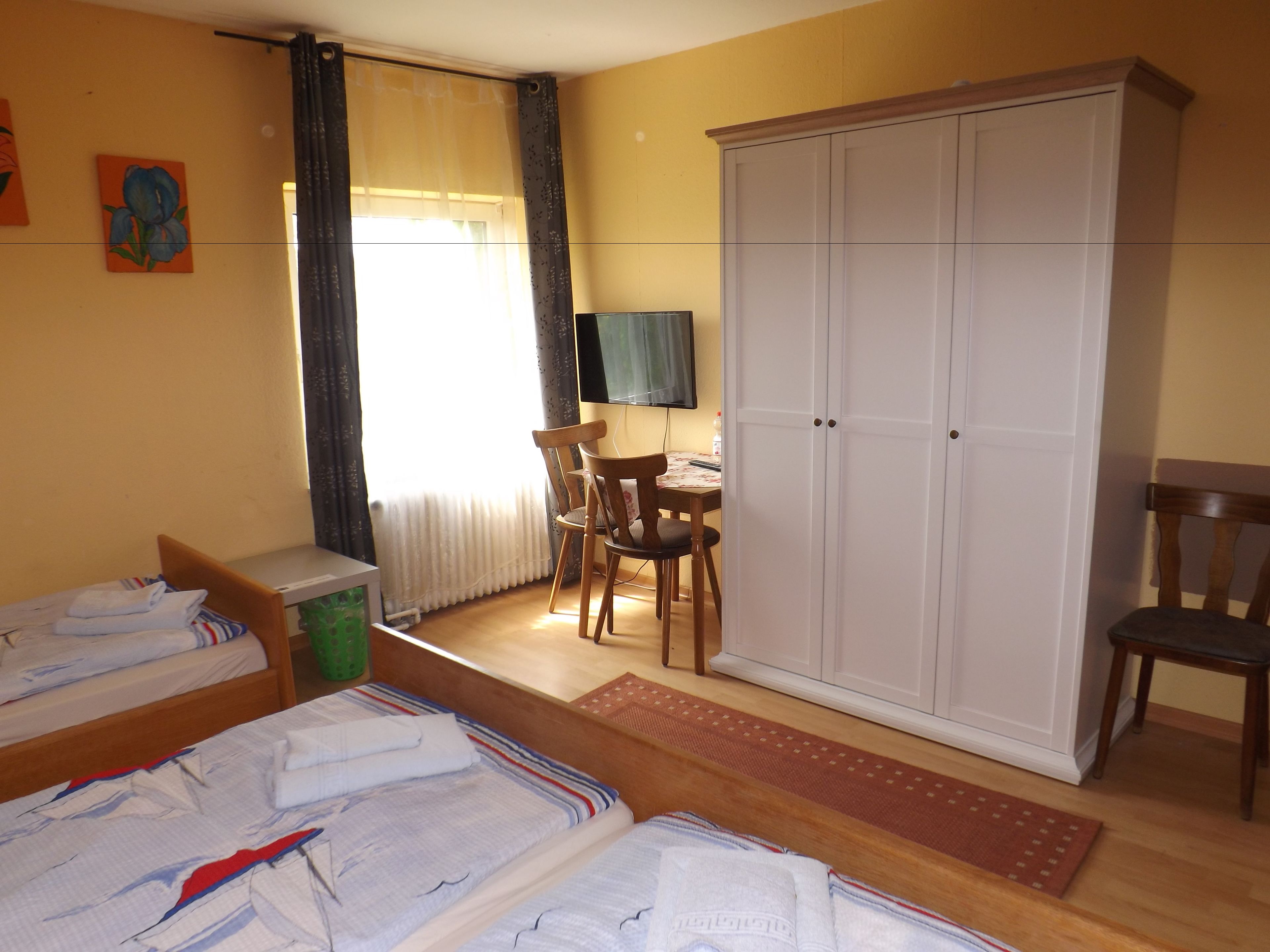 A room with two beds, a desk with a chair, a wardrobe, and a radiator.