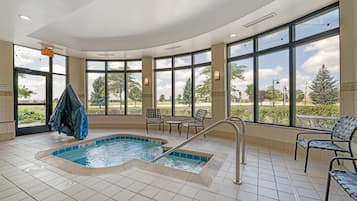 Un área de piscina con jacuzzi, sillas y grandes ventanales que ofrecen vistas al exterior.