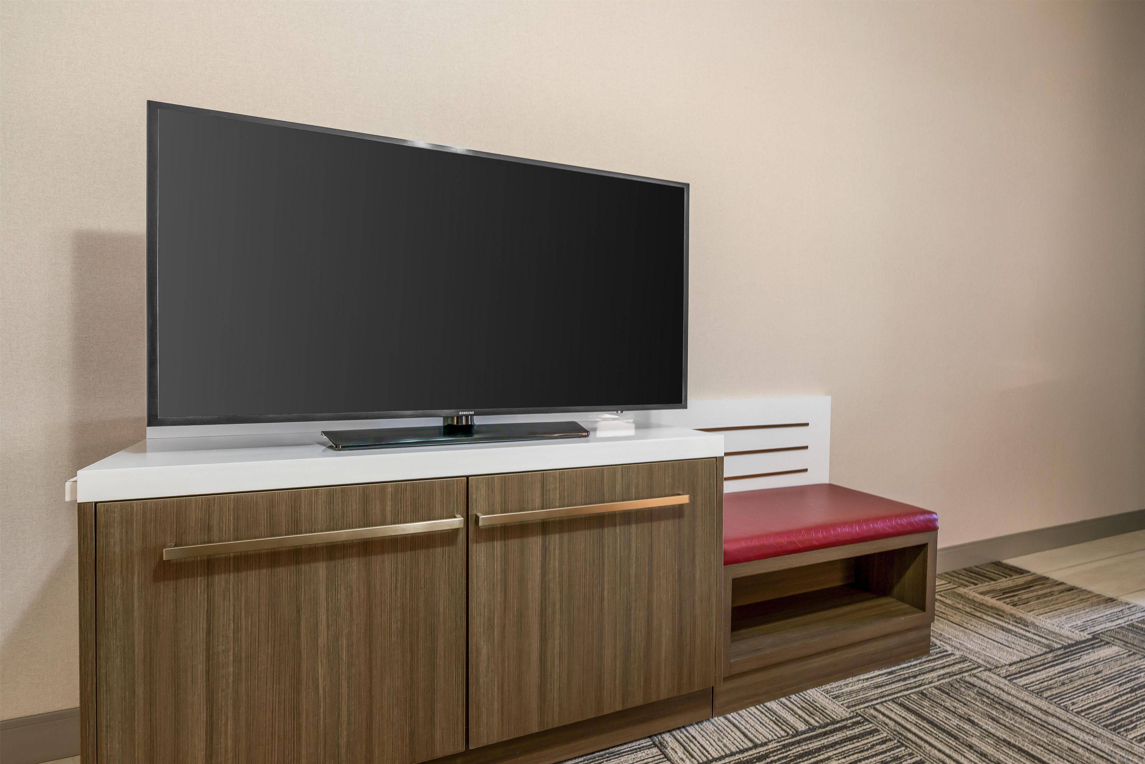 Een flatscreen televisie op een wit kastje met een houten afwerking en een rode, beklede bank.