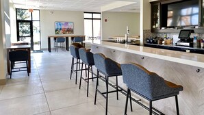 A modern bar area with a counter, stools, and a television. - Hilton Garden Inn Oconomowoc (Oconomowoc)