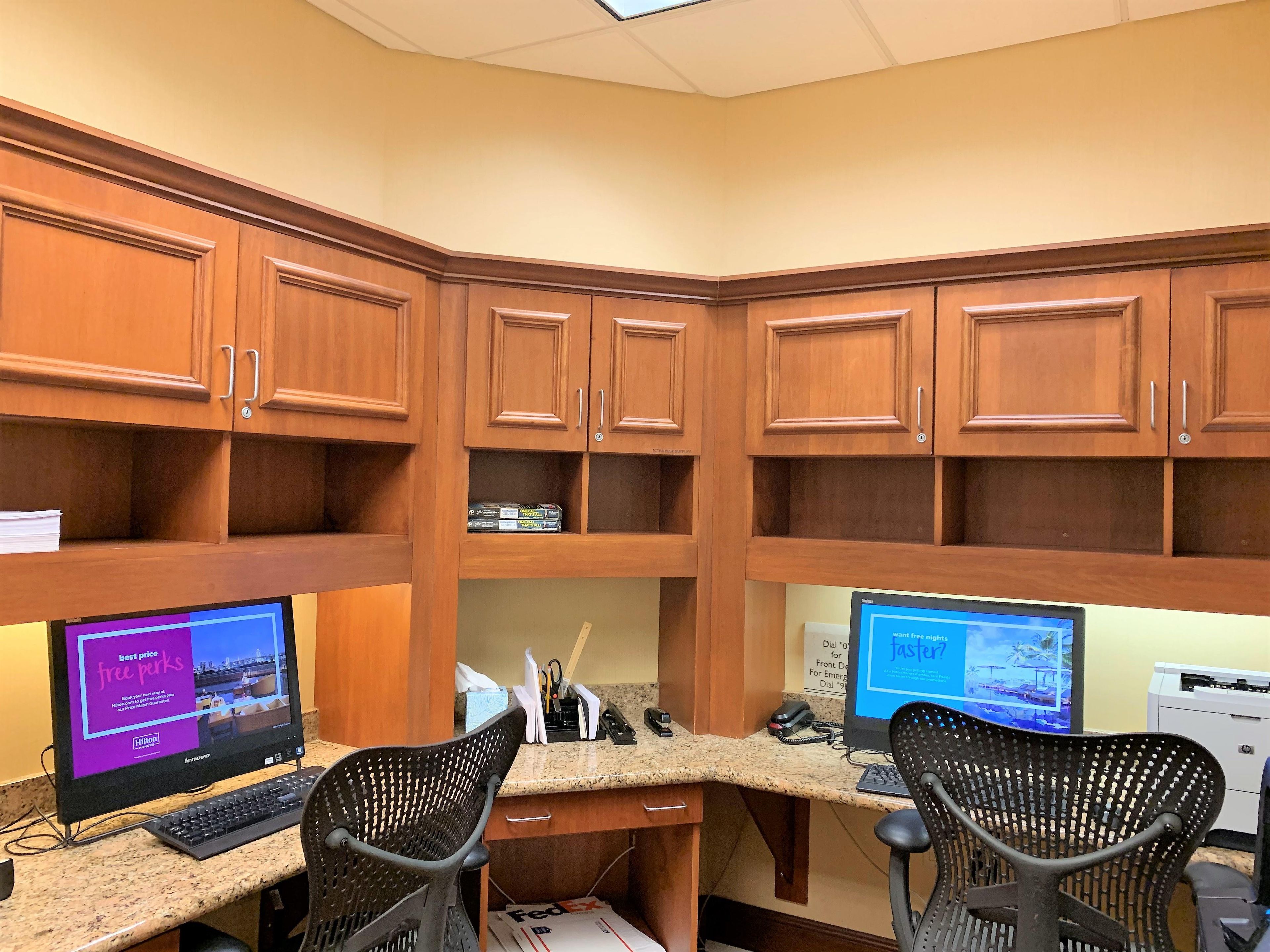 A hotel room with wooden cabinets, two desks with computers, and two office chairs.