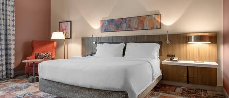 A hotel room with a large bed, a chair, a bedside table, a lamp, and a painting on the wall.