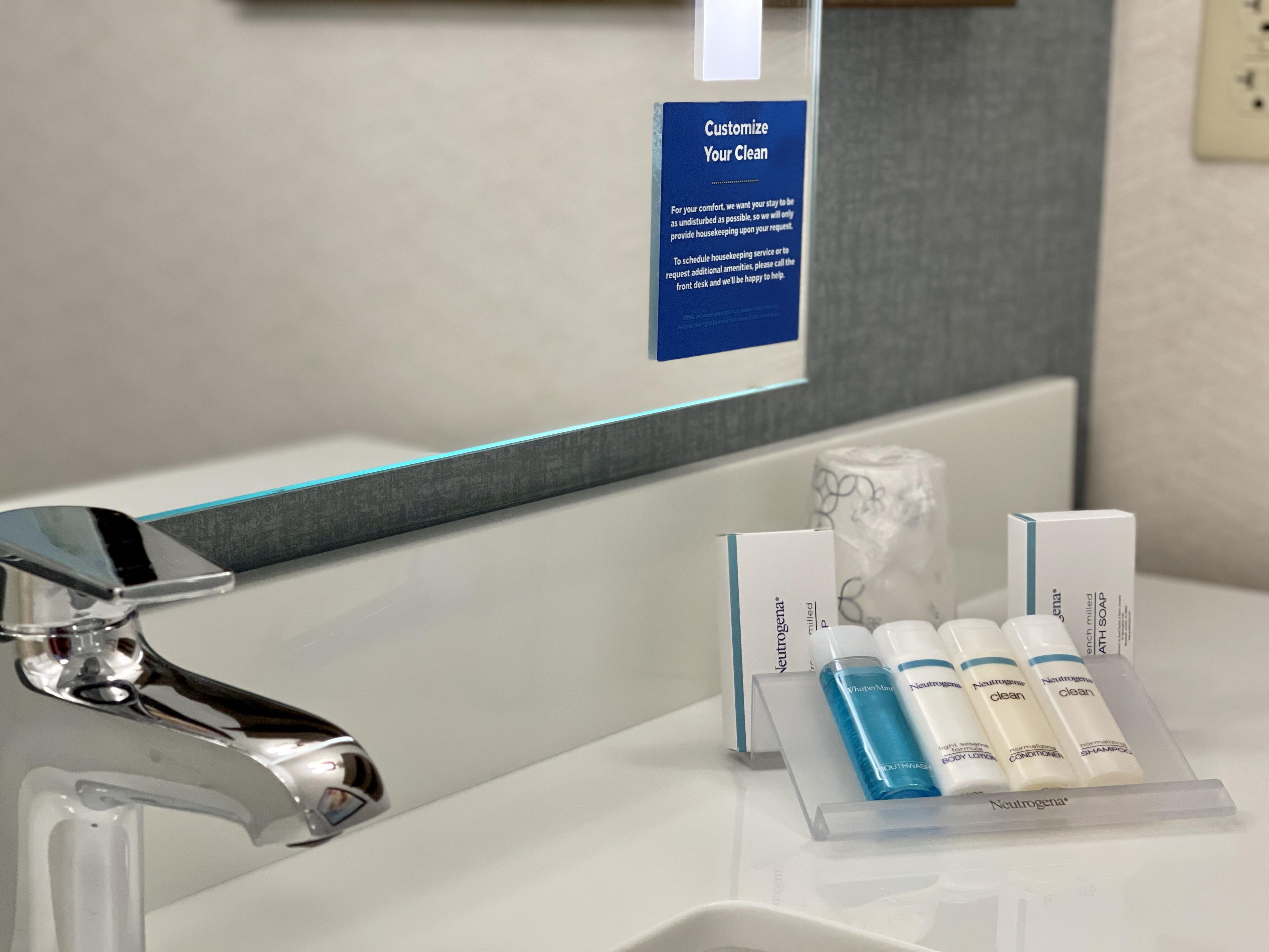A bathroom with a modern faucet, a sign offering customizable cleaning services, and a display of Neutrogena personal care products.