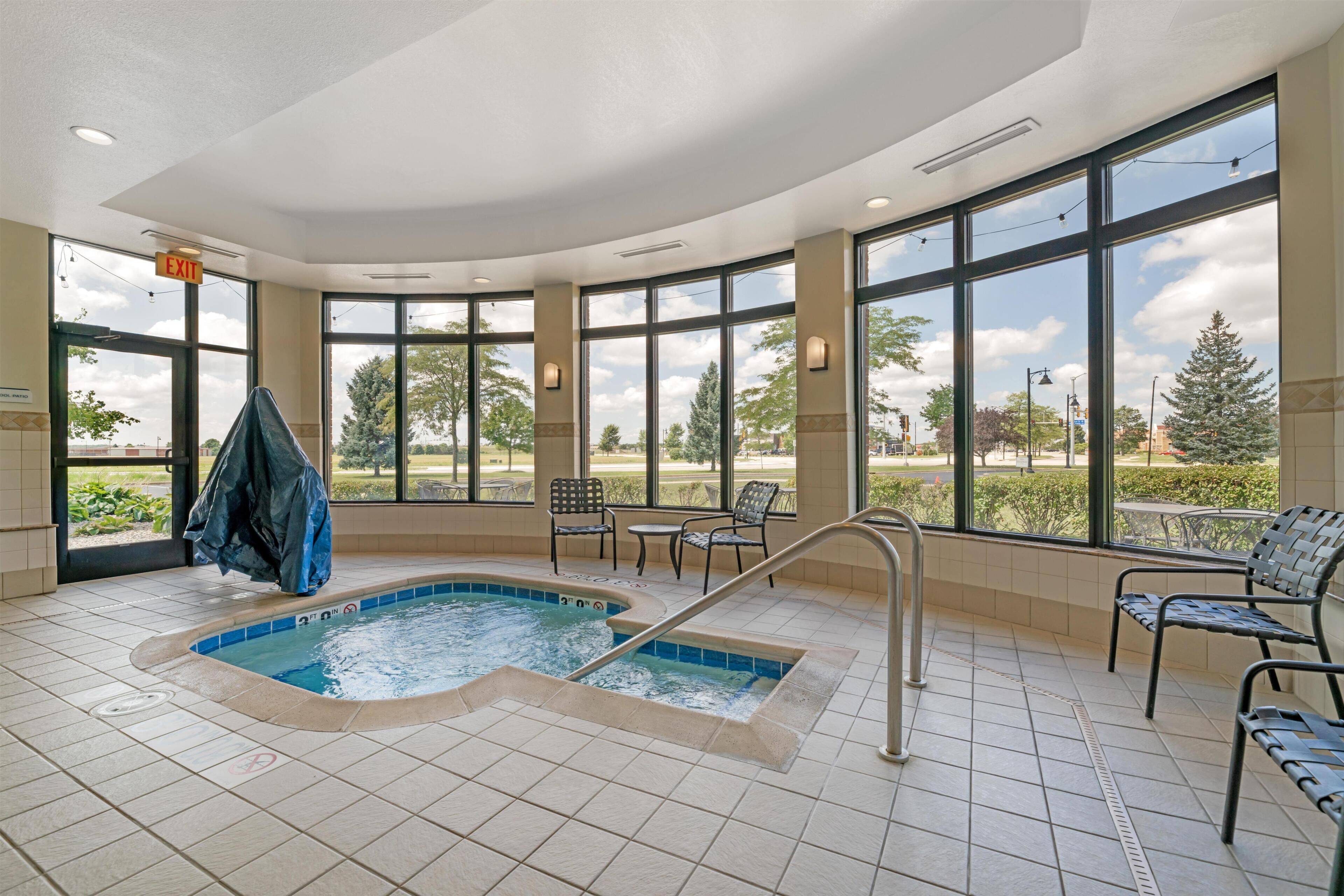 Ein Poolbereich mit Whirlpool, Liegestühlen und großen Fenstern mit Blick ins Freie.