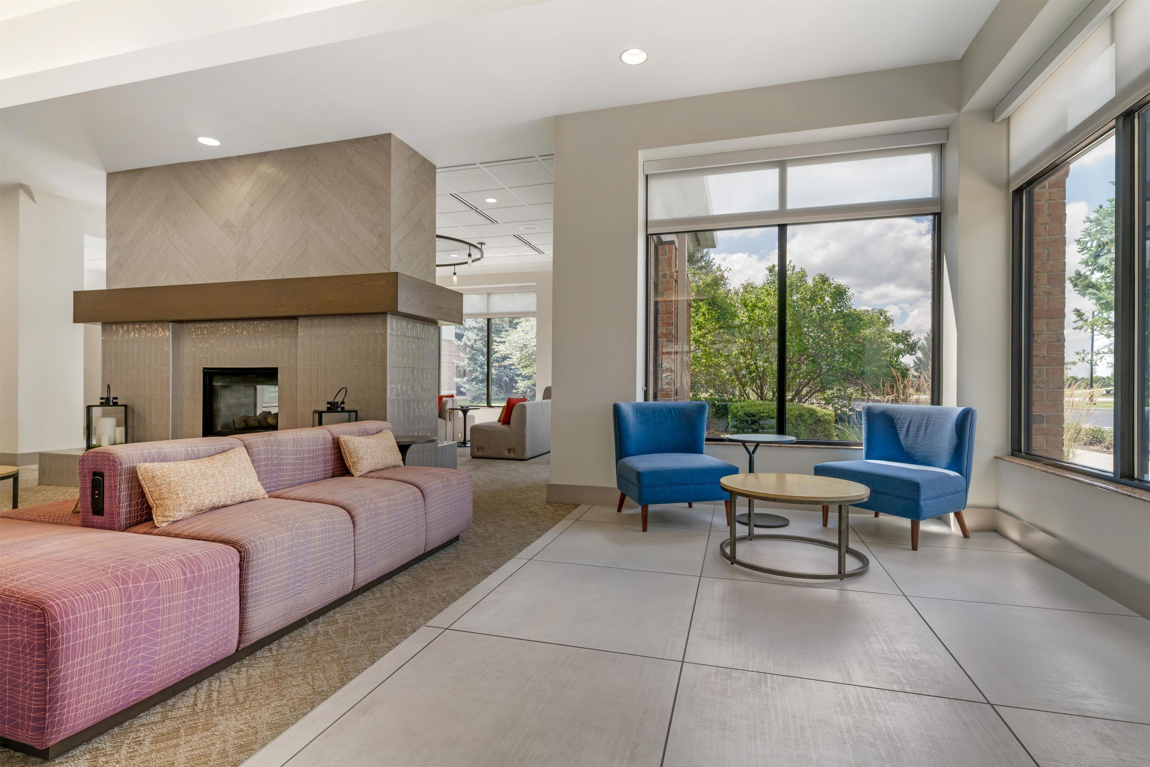 A modern living room with a fireplace, sofas, and a large window offering a view of the outdoors.