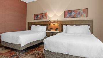 A hotel room with two beds, a nightstand, a wall-mounted lamp, and abstract paintings.