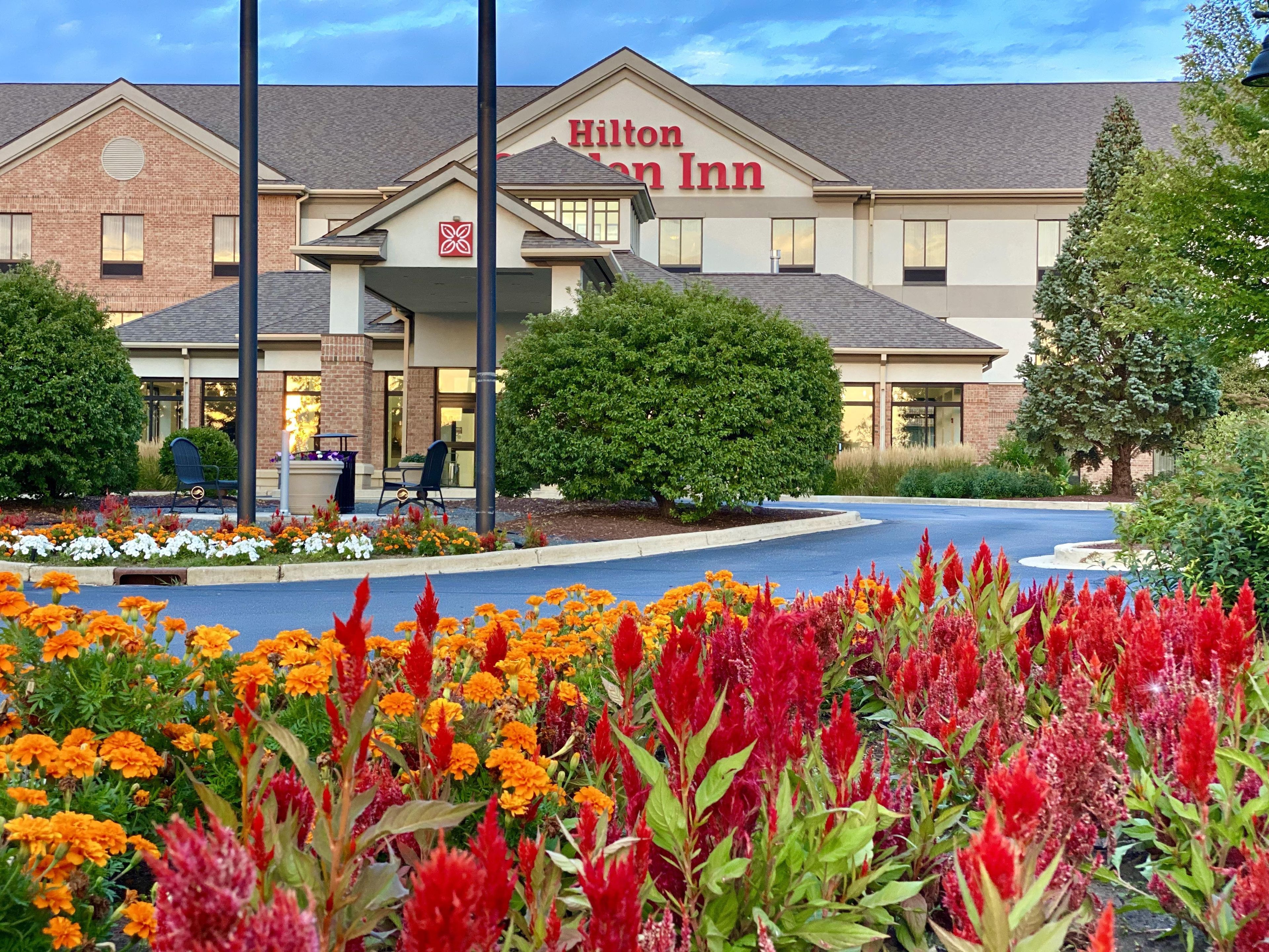 A Hilton Inn hotel with a brick facade, a covered entrance, and a landscaped garden with colorful flowers.