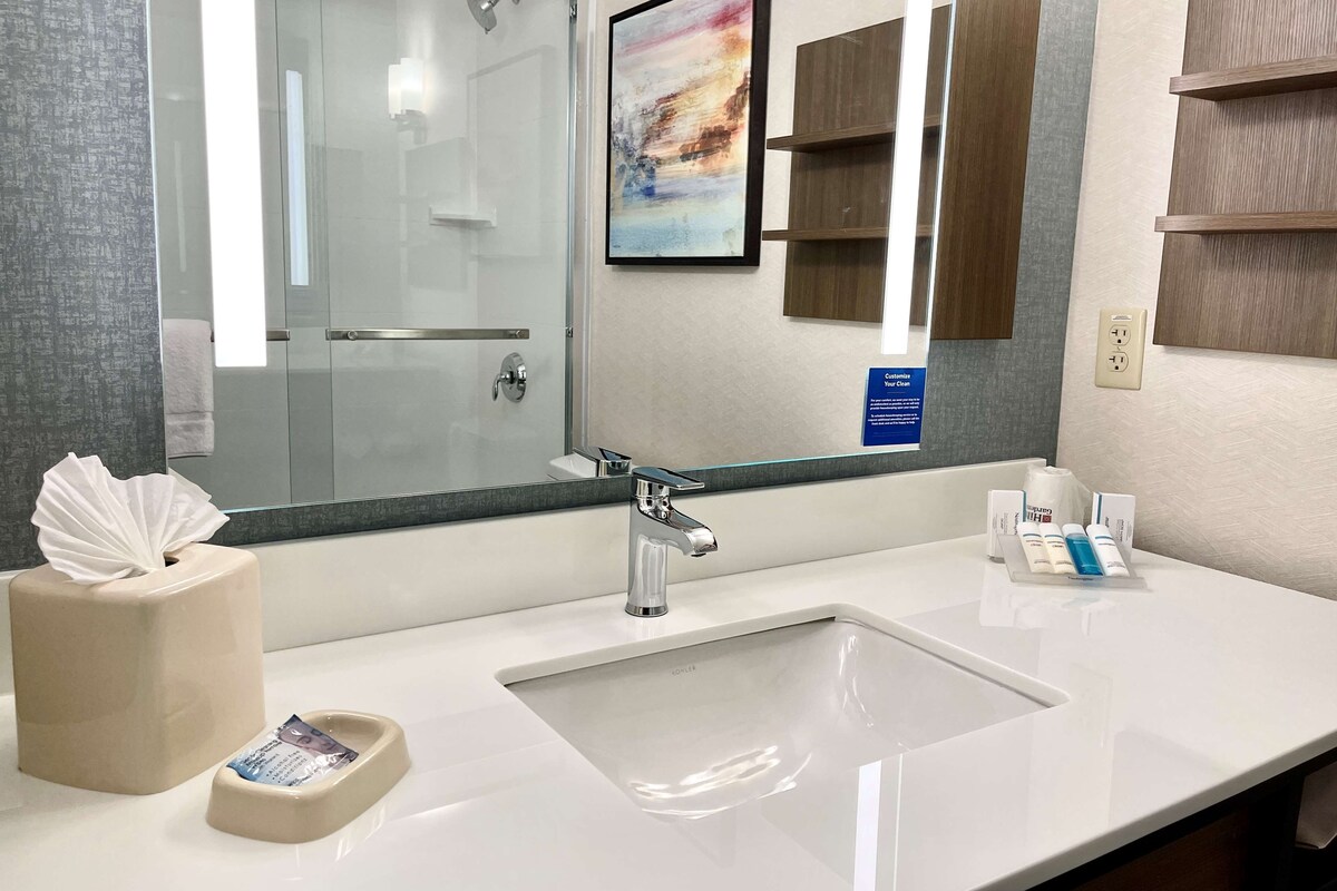 A modern bathroom with a large mirror, a glass shower enclosure, and a white sink.