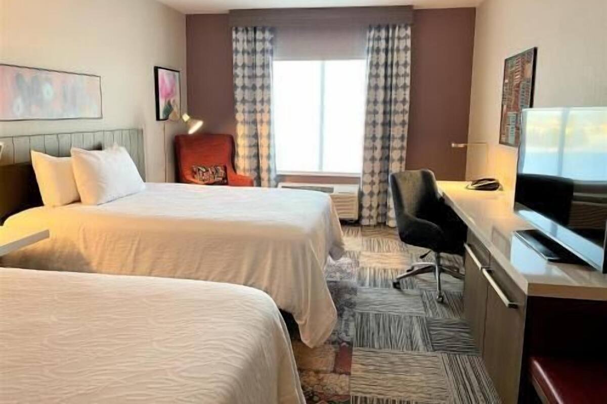 A hotel room with two beds, a desk with a chair, a television, and a window with curtains.