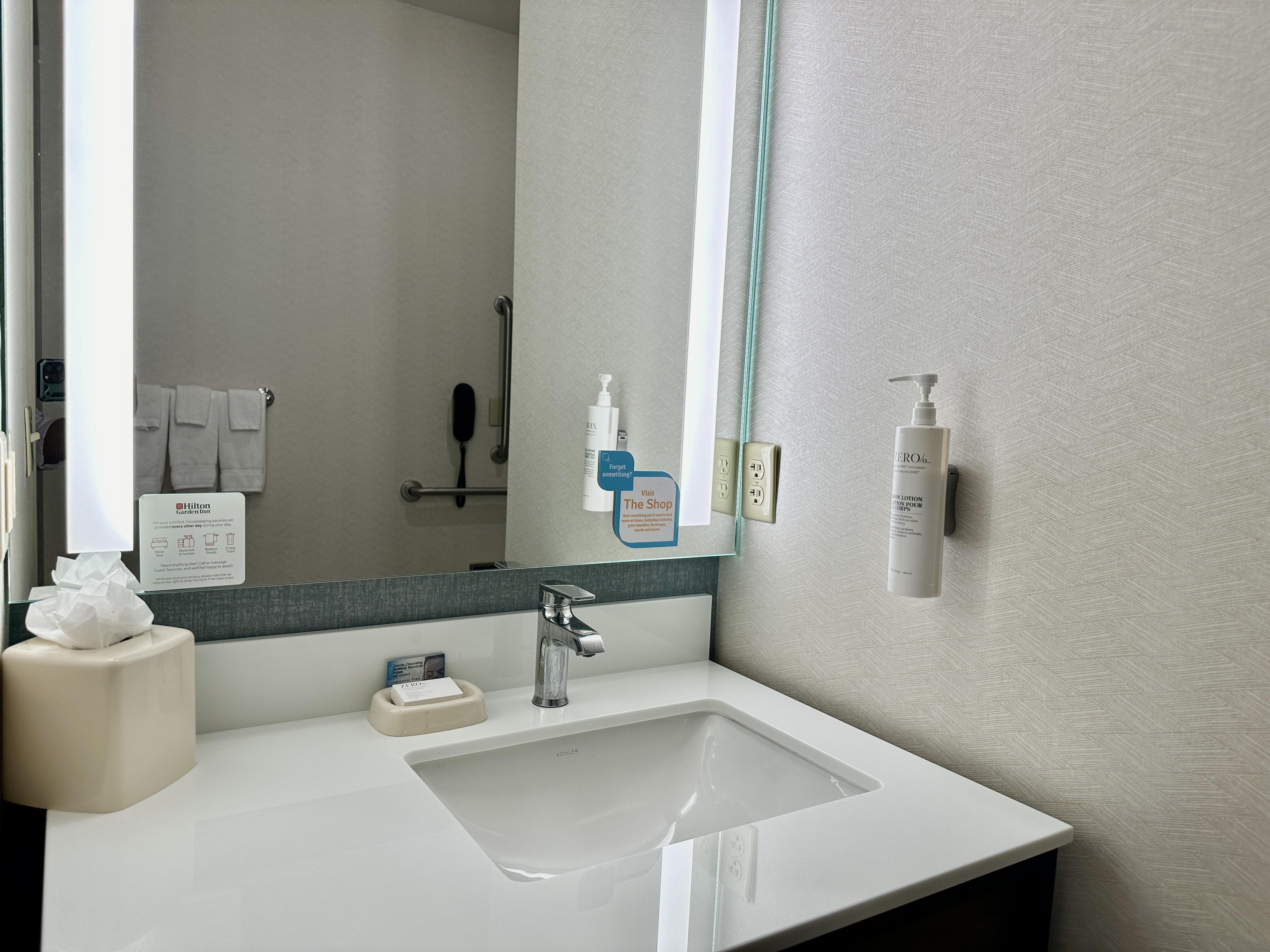 A hotel bathroom with a sink, mirror, towel rack, and toiletries.