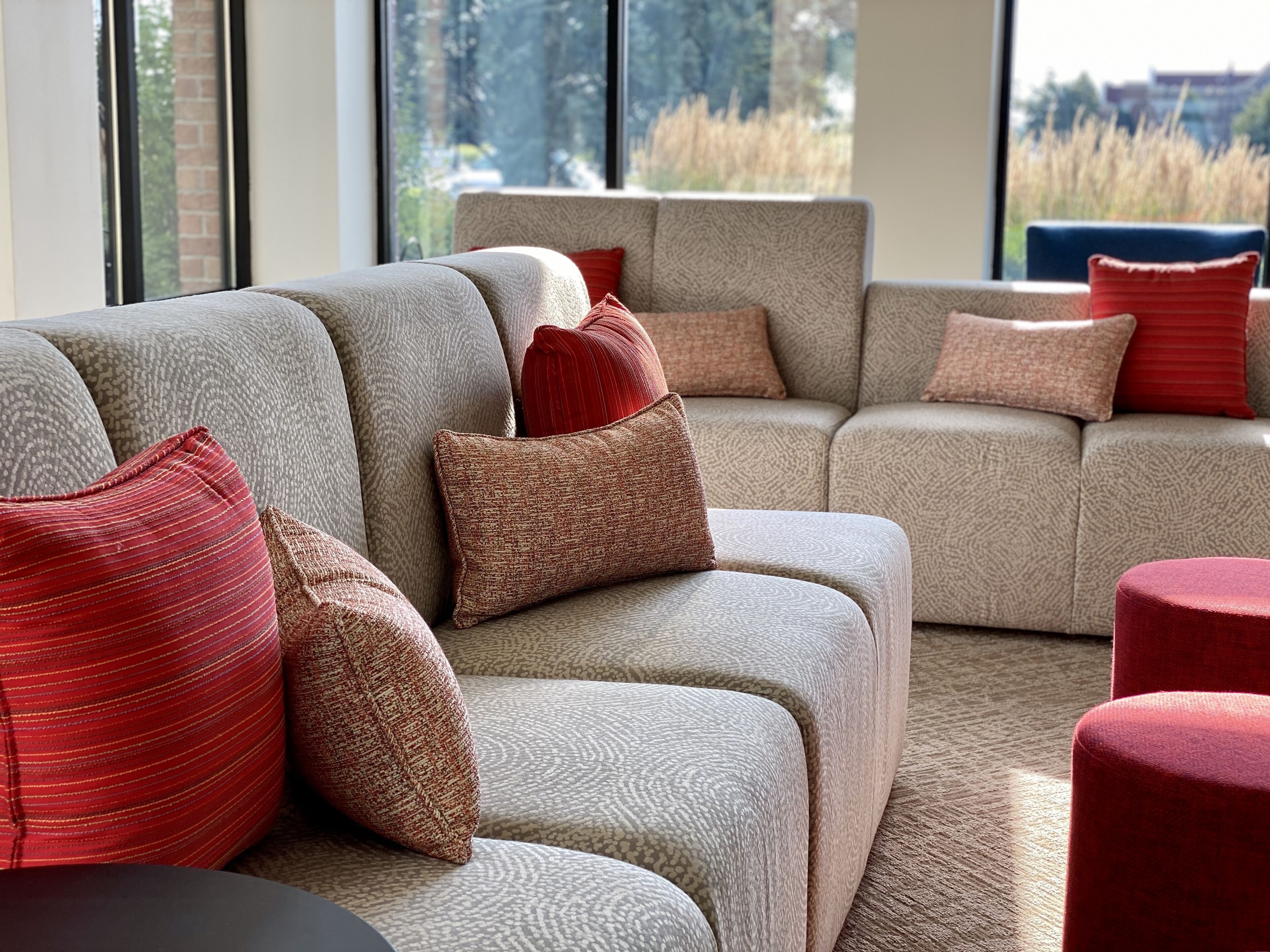 A modern living room with a sectional sofa and a red ottoman.