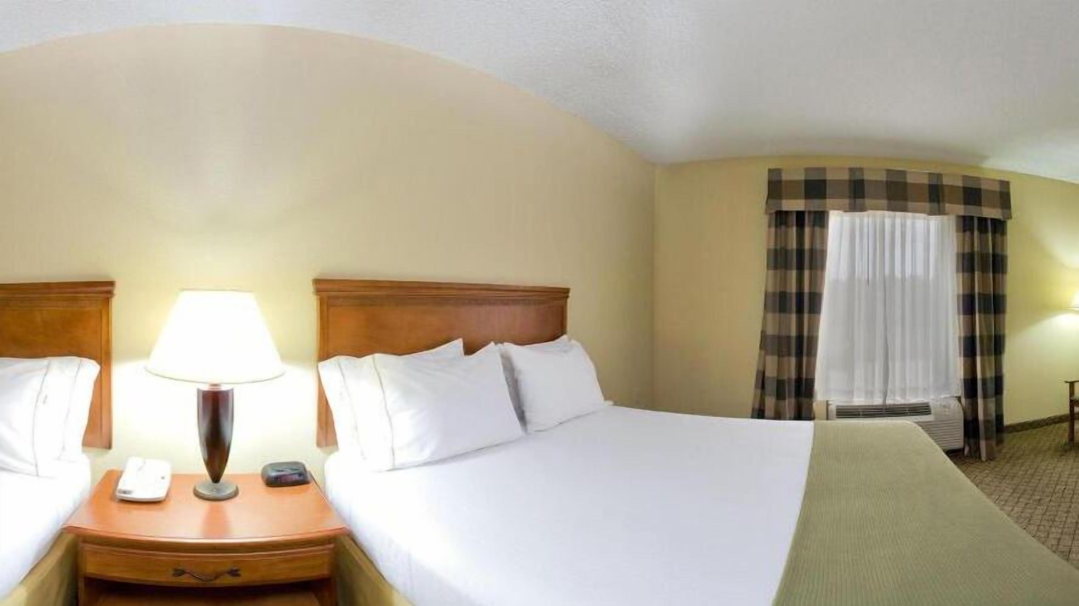 A hotel room with two beds, a bedside table with a lamp, a telephone, and a check-in station.