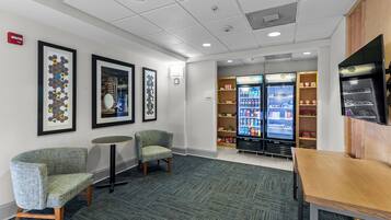 A lobby with seating, a vending machine, and a wall-mounted fire alarm.
