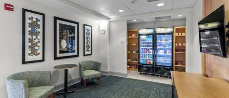 A lobby with seating, a vending machine, and a wall-mounted fire alarm.