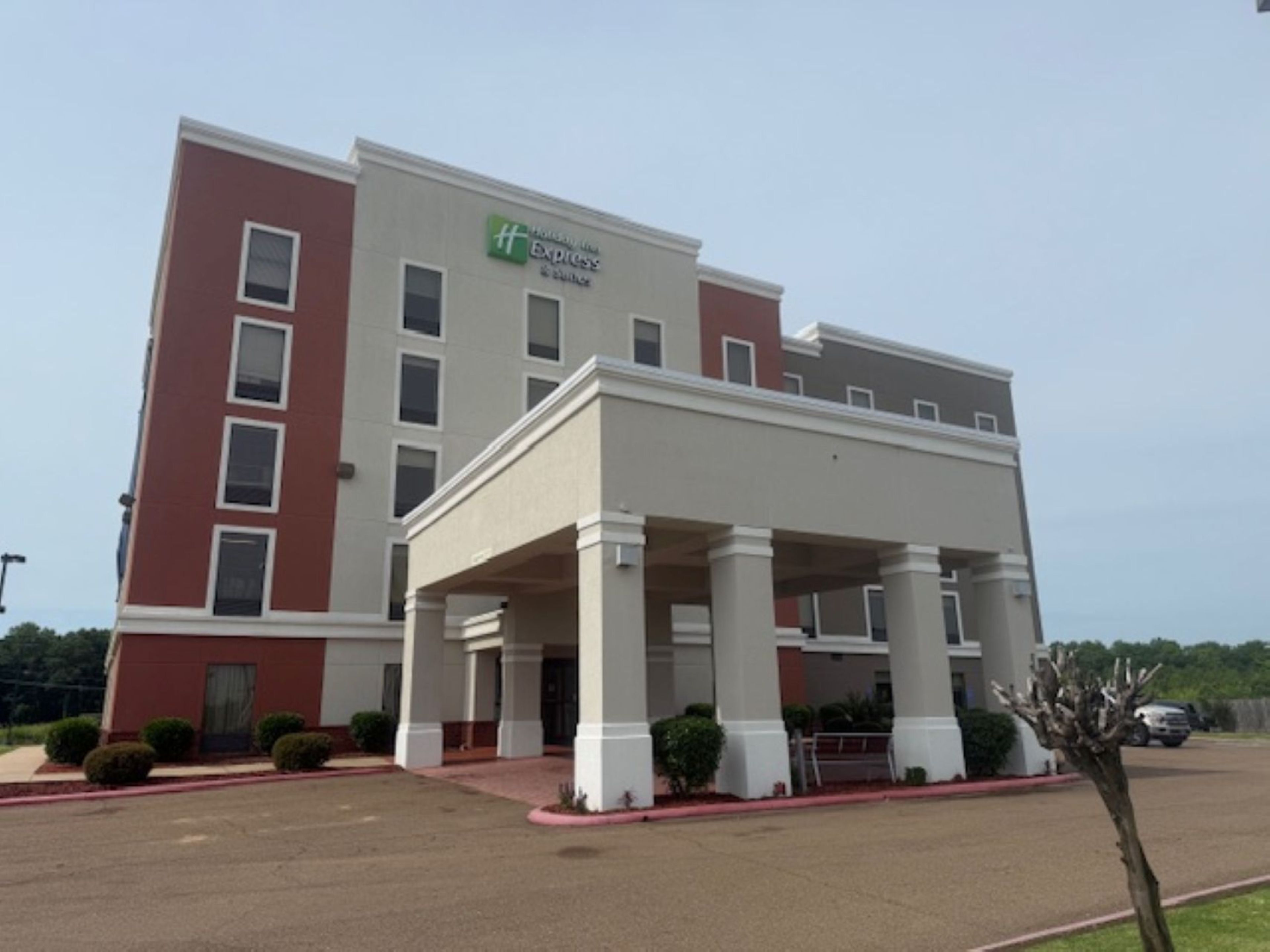 A hotel with a red and white facade, a covered entrance with columns, and a parking lot.