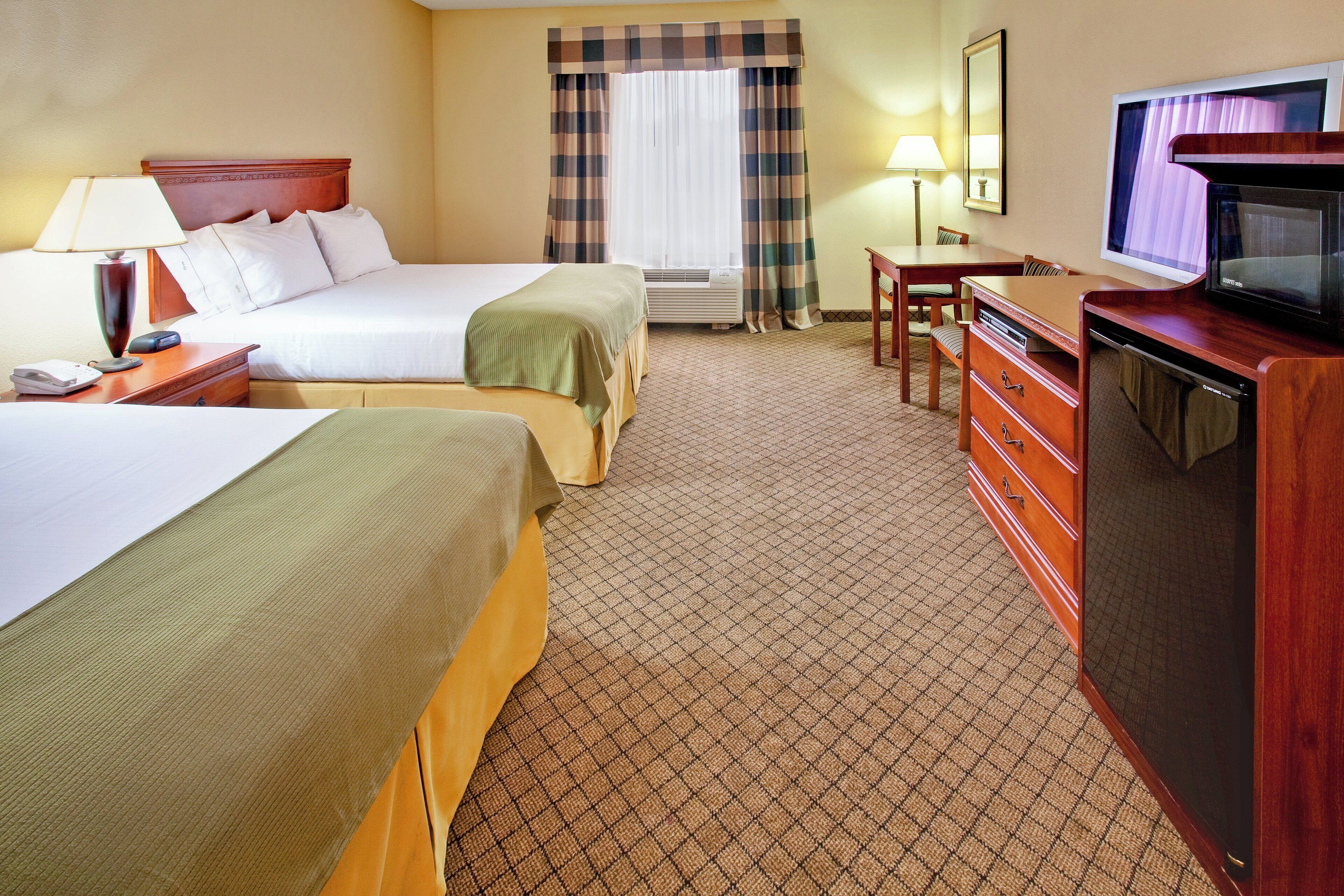 A hotel room with two beds, a desk, a television, and a dresser.