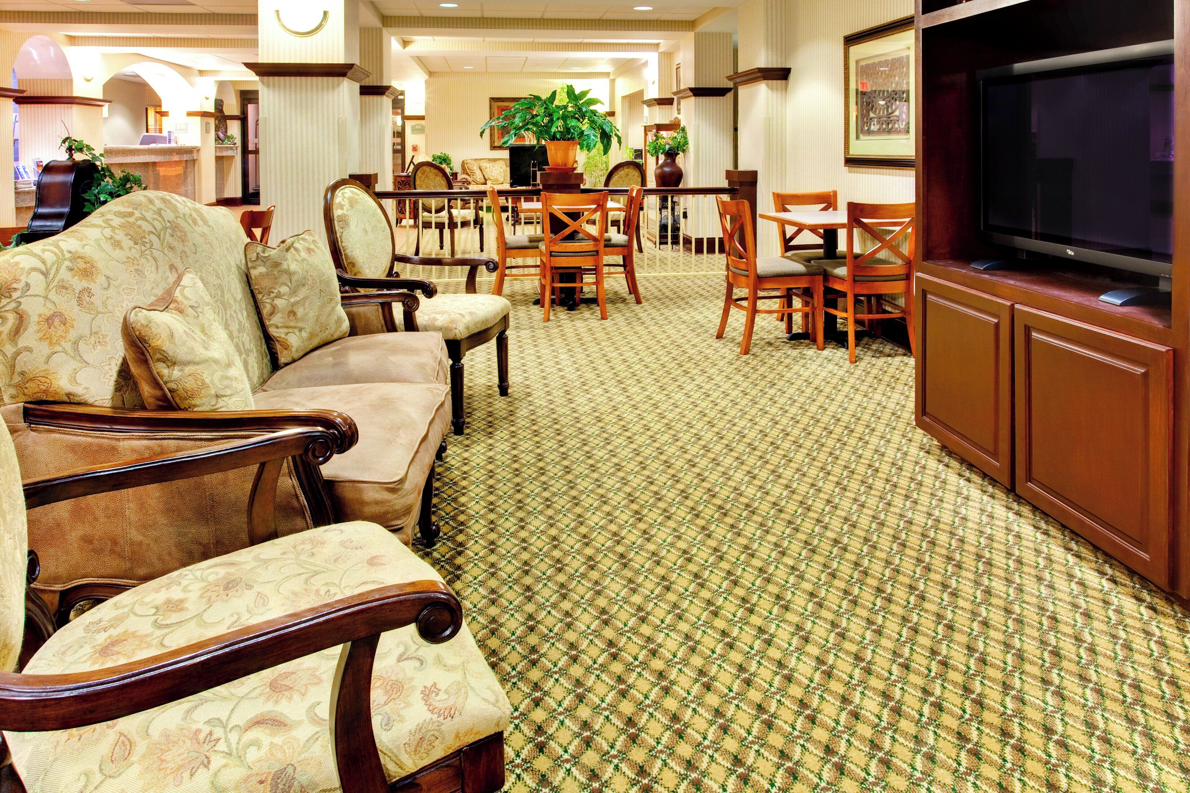 Un vestíbulo de hotel con un sofá, sillas, un televisor y una alfombra estampada.