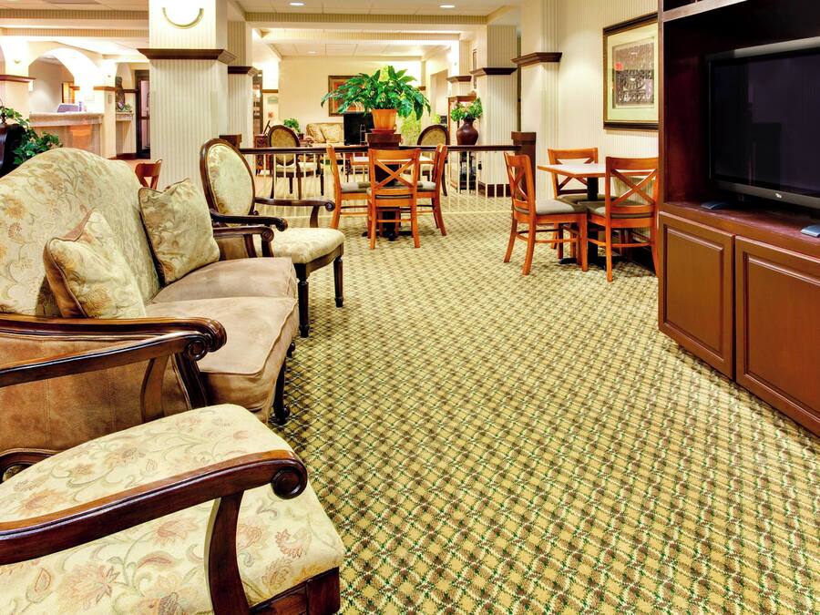 Un vestíbulo de hotel con un sofá, sillas, un televisor y una alfombra estampada.