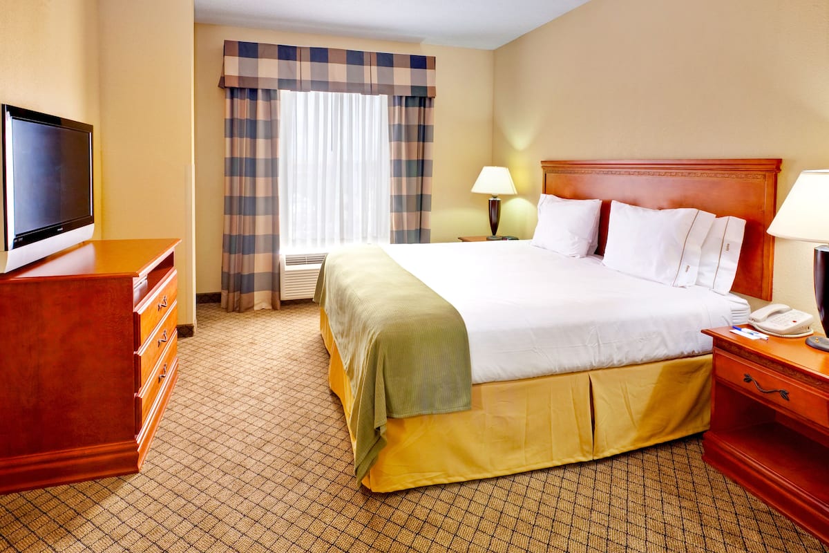 A hotel room with a large bed, a television, a dresser, and a window with curtains.