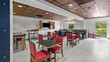 Restaurante moderno com painéis de teto em madeira, TV de tela plana e uma combinação de cadeiras estofadas em vermelho e azul.