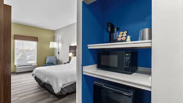 Habitación de hotel con cama, escritorio, microondas, cafetera y refrigerador pequeño.