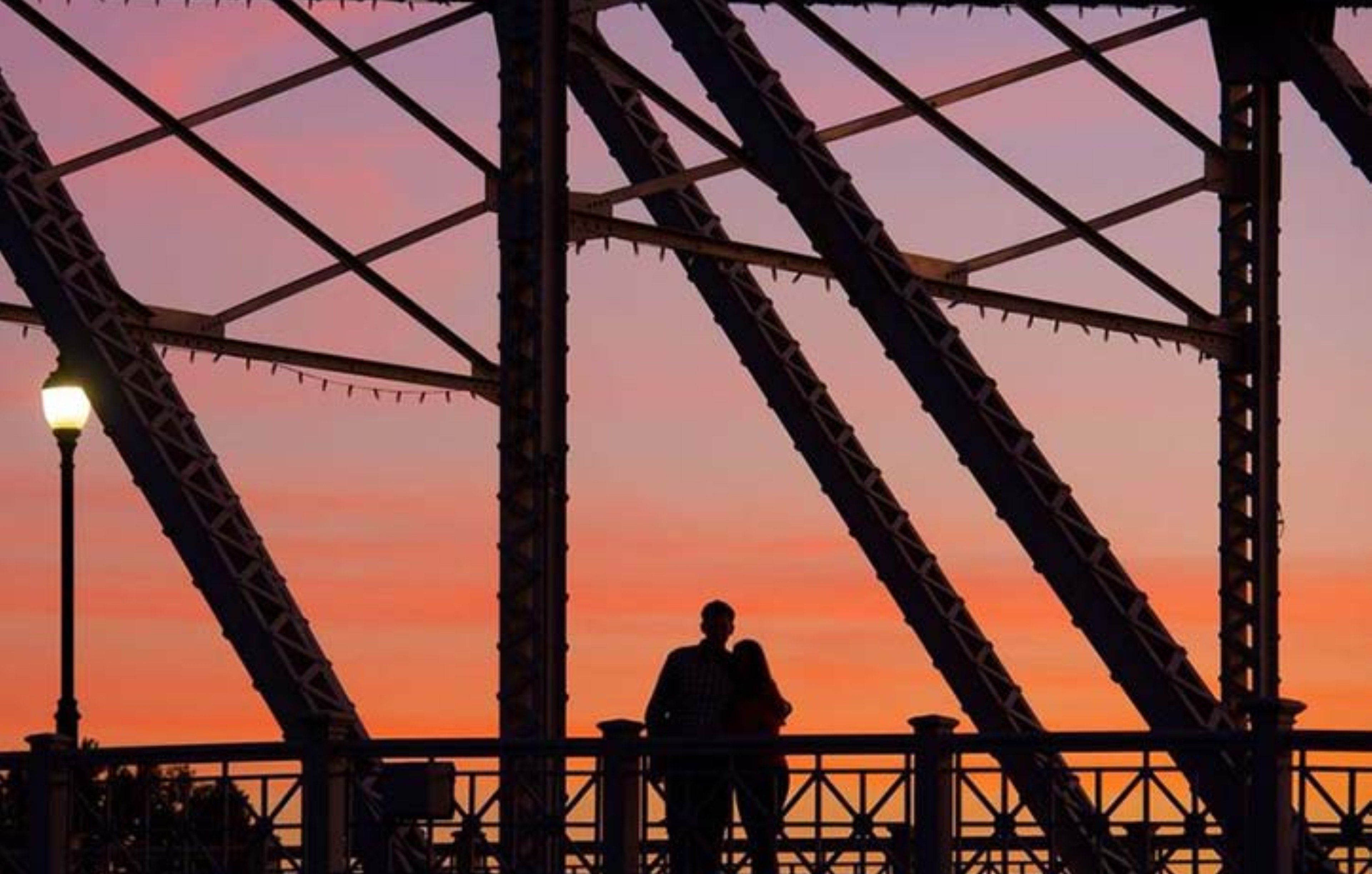 La silhouette d’une personne se tenant sous un pont, avec un coucher de soleil en arrière-plan.