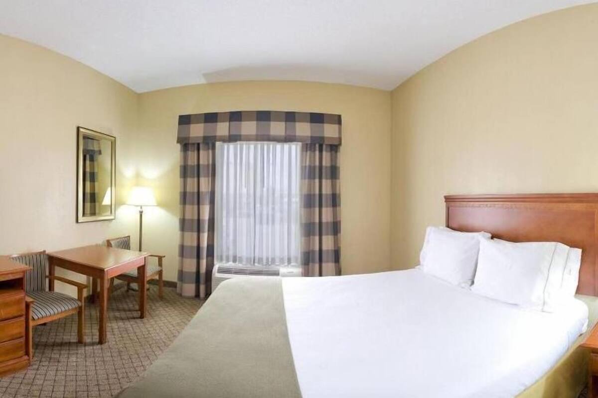 A hotel room with a bed, a desk, a chair, a lamp, and a window with curtains.