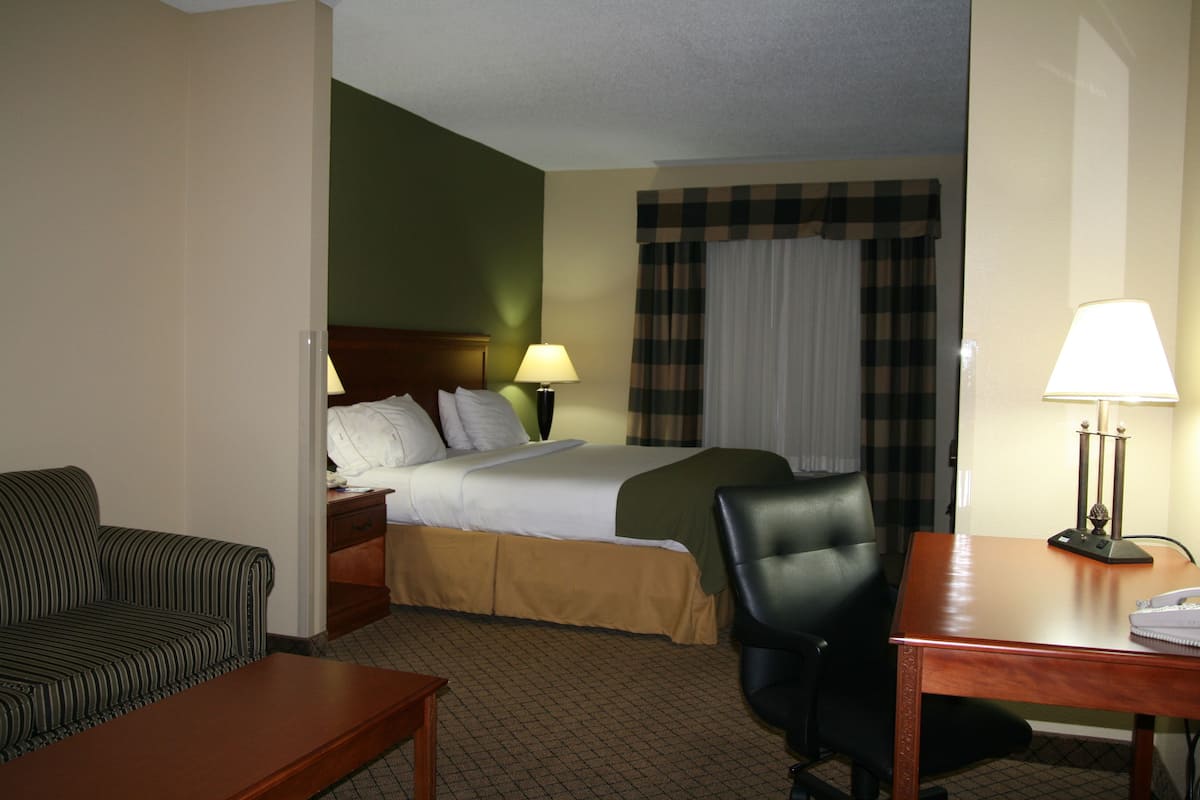 A hotel room with a bed, a desk, a chair, a sofa, and a lamp.