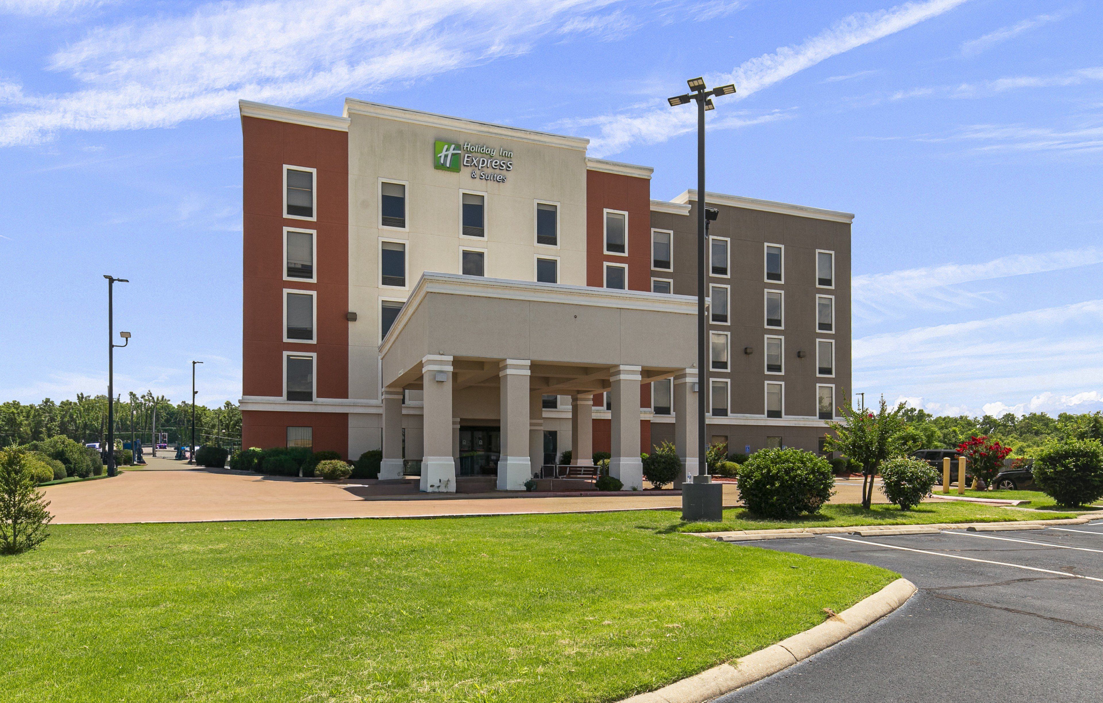 A Holiday Inn Express & Suites building with a covered entrance, multiple windows, and a parking lot.