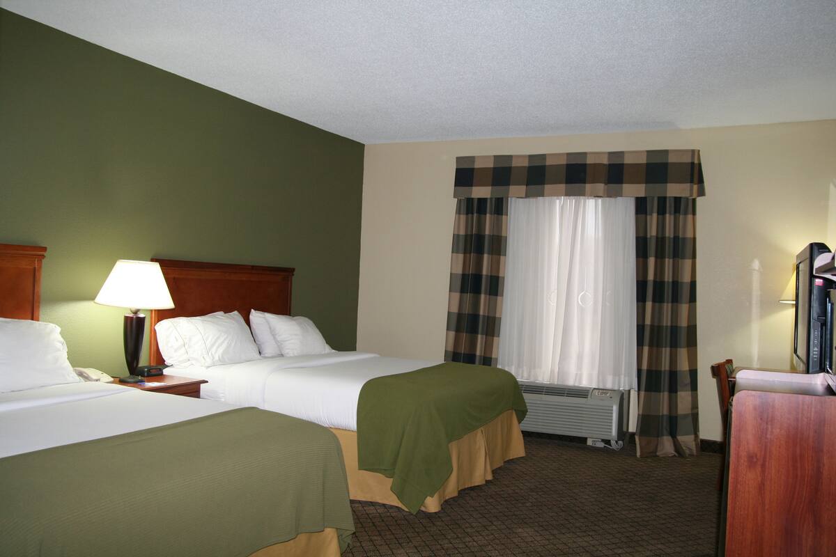 A hotel room with two beds, a desk, a lamp, a television, and a window with curtains.