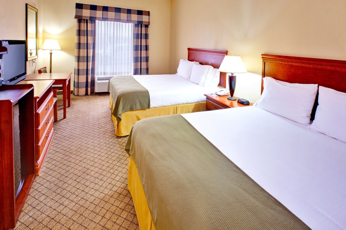 A hotel room with two beds, a desk, a television, and a window with curtains.
