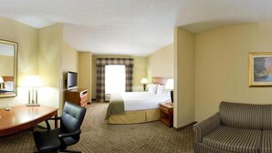 A hotel room with a bed, a desk with a chair, a television, a sofa, and a painting on the wall. - Holiday Inn Express & Suites - Greenwood by IHG (Greenwood)