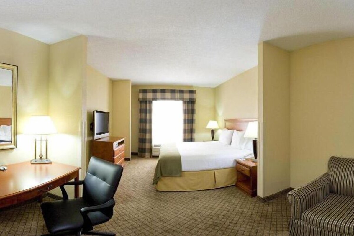 A hotel room with a bed, a desk with a chair, a television, a sofa, and a painting on the wall.