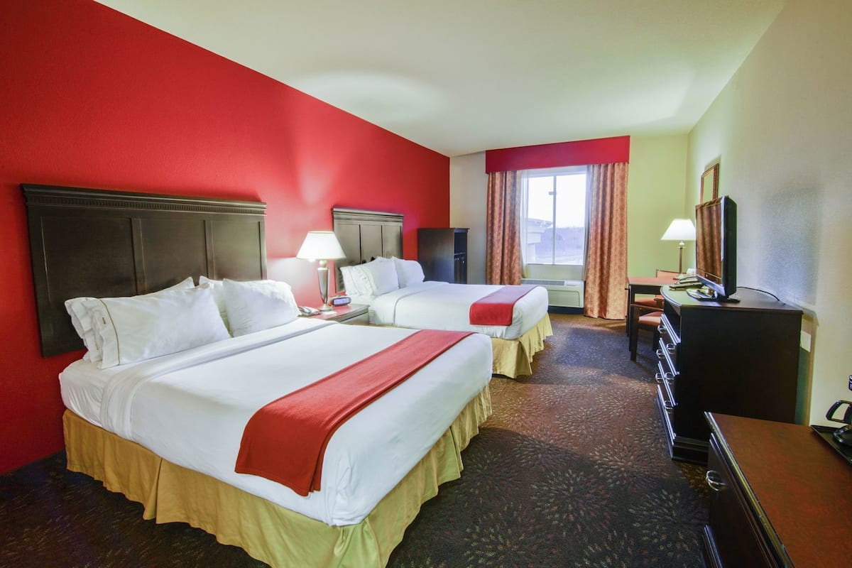 A hotel room with two beds, a desk, a television, and a window with curtains.