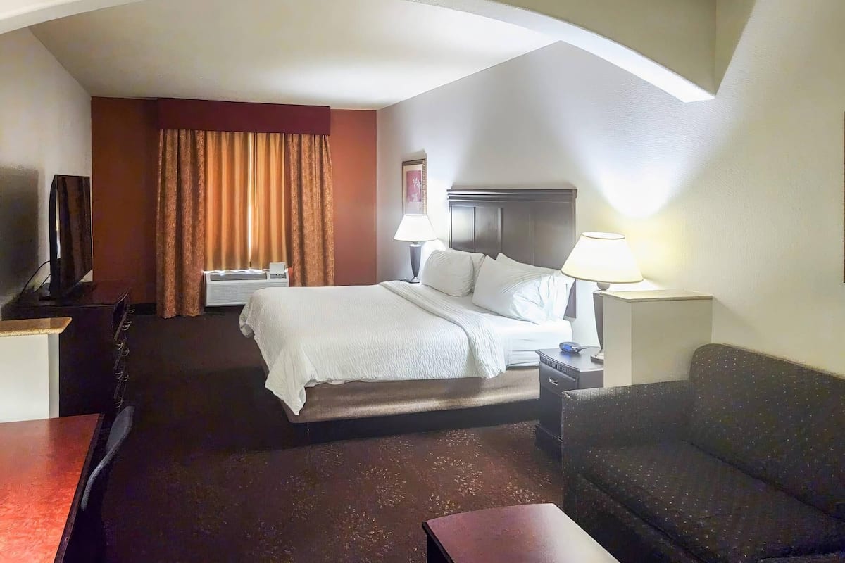 A hotel room with a bed, a desk, a television, a sofa, and a window with curtains.