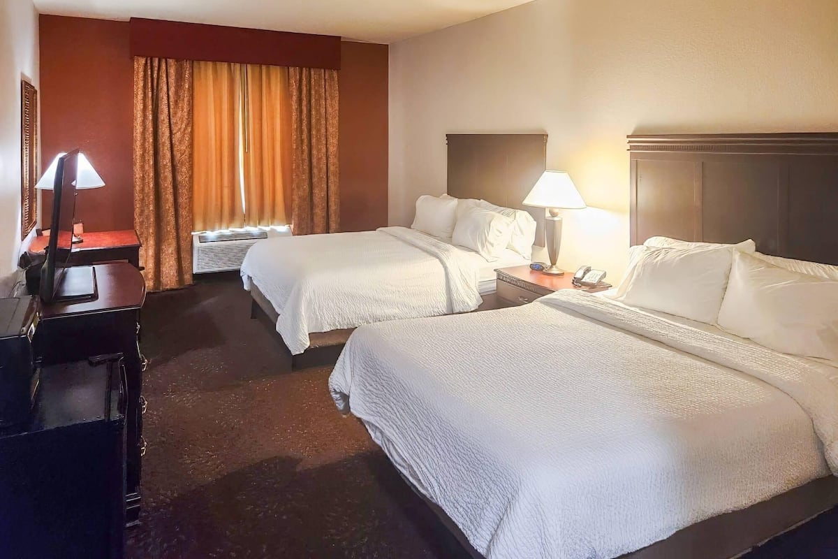 A hotel room with two beds, a desk with a lamp, a telephone, and a window with curtains.