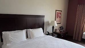 A hotel room with a large bed, a nightstand with a lamp, a painting on the wall, and a window with curtains. - Country Inn & Suites by Radisson, Terrell (Terrell)