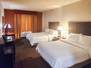 A hotel room with two beds, a desk with a lamp, a telephone, and a window with curtains.