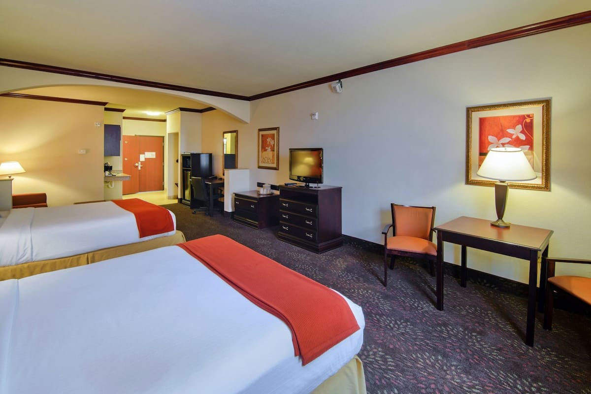 A hotel room with two beds, a desk, a chair, a television, and a desk lamp.