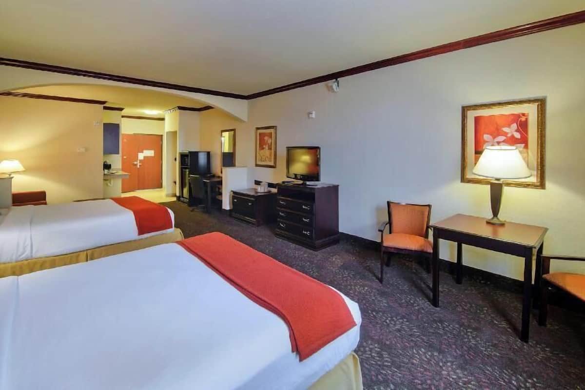 A hotel room with two beds, a desk, a chair, a television, and a desk lamp.