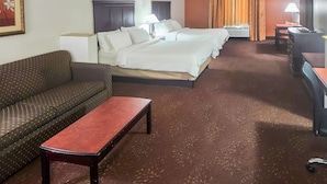 A hotel room with a sofa, a small table, a bed with two pillows, a desk with a lamp, and a television. - Country Inn & Suites by Radisson, Terrell (Terrell)